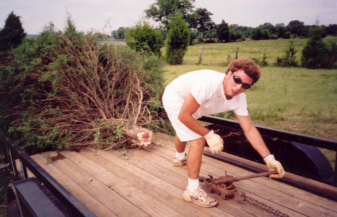 Michael Woodfin uses a come-a-long to pull a cedar tree on the trailer.  